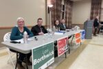 Green Party candidate Lori Borthwick, Liberal candidate David O'Neil, NDP candidate Amanda Robertson, and Progressive Conservative candidate Tyler Allsopp sit at a table, with their respective political signs in front, waiting for the meeting to start.